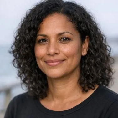 Woman in her early forties, dark curly hair, warm brown skin, calm expression